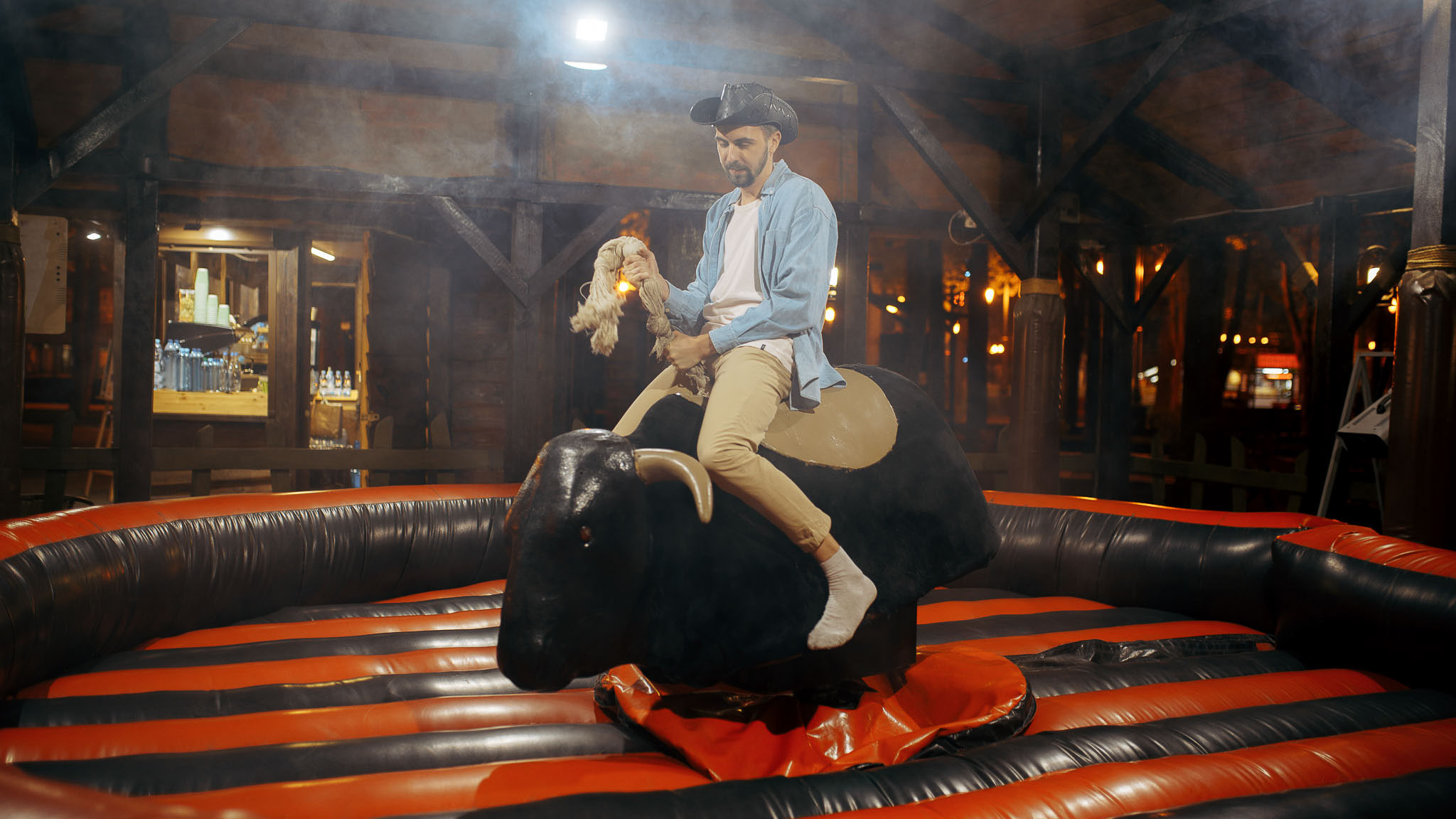 Man i cowboyhatt rider en mekanisk tjur inomhus.