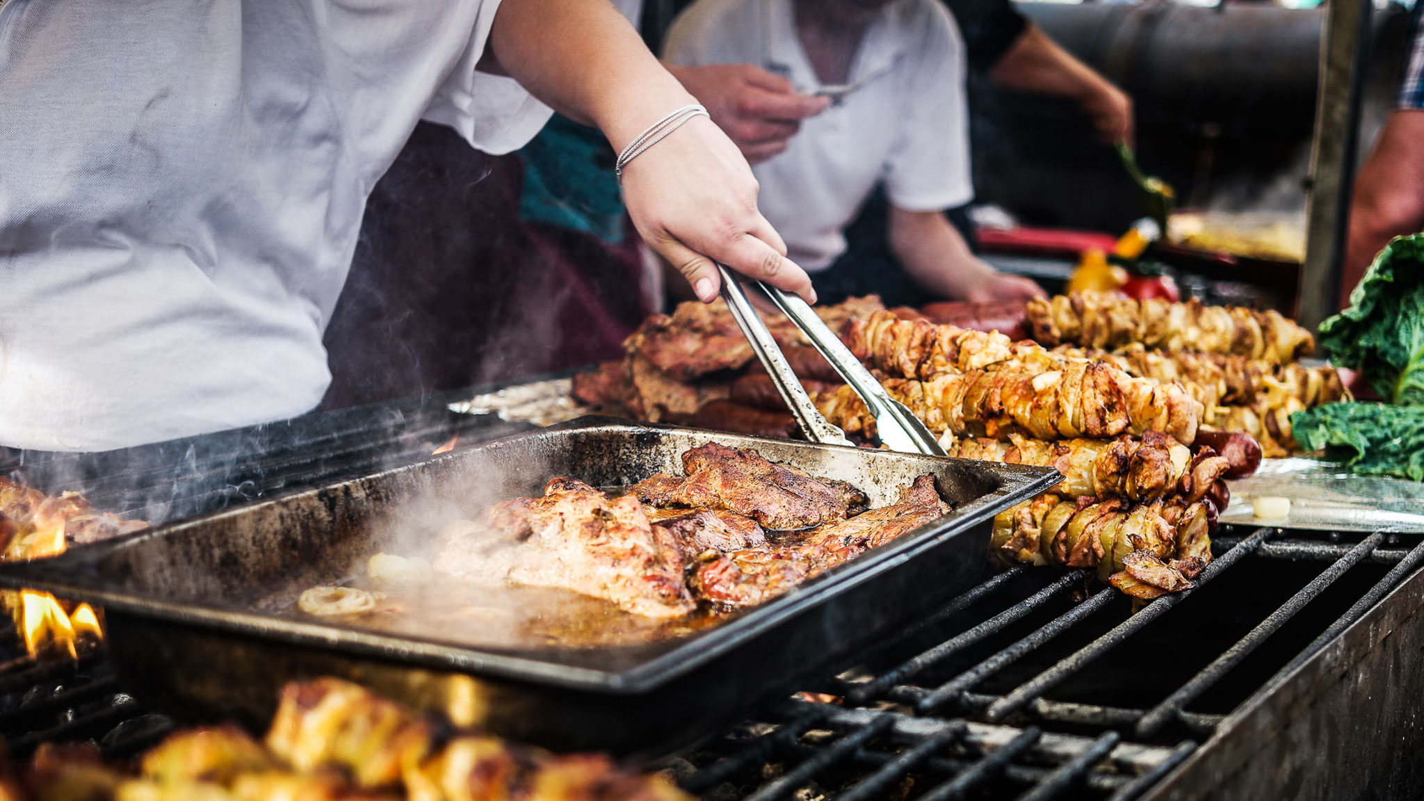 Person grillar kött och spett över öppen eld vid ett serveringsstånd.
